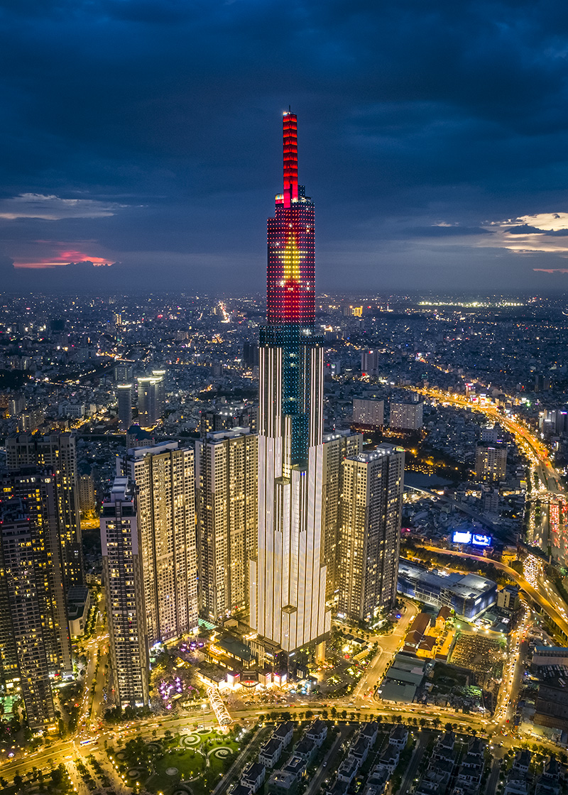 An aerial view of a modern city skyline at dusk, with illuminated buildings and a river.